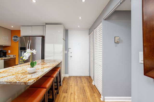 kitchen with light stone counters, appliances with stainless steel finishes, light wood-type flooring, a kitchen bar, and modern cabinets