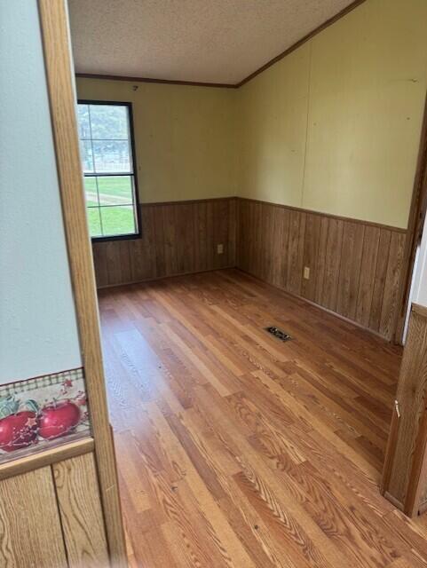 6201 N Lakeshore Rd, Deckerville, MI 48427 - empty room featuring light wood-style flooring, a textured ceiling, a wainscoted wall, crown molding, and wood walls