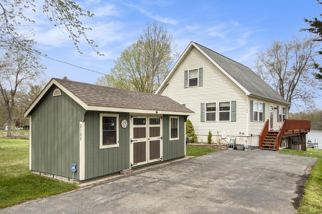 back of property featuring an outdoor structure, roof with shingles, a wooden deck, and a storage shed