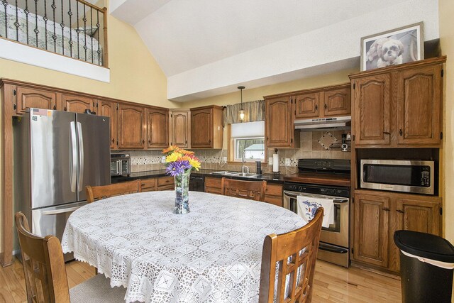 kitchen with decorative backsplash, a sink, under cabinet range hood, stainless steel appliances, and light wood-style flooring
