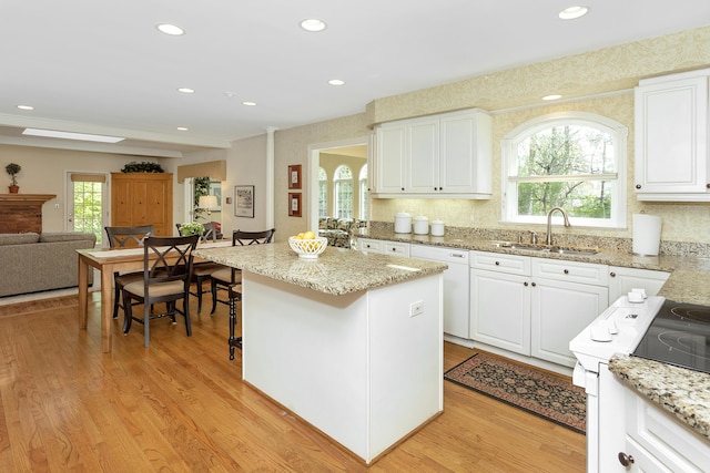 kitchen with light stone countertops, a sink, light wood finished floors, white cabinetry, and open floor plan