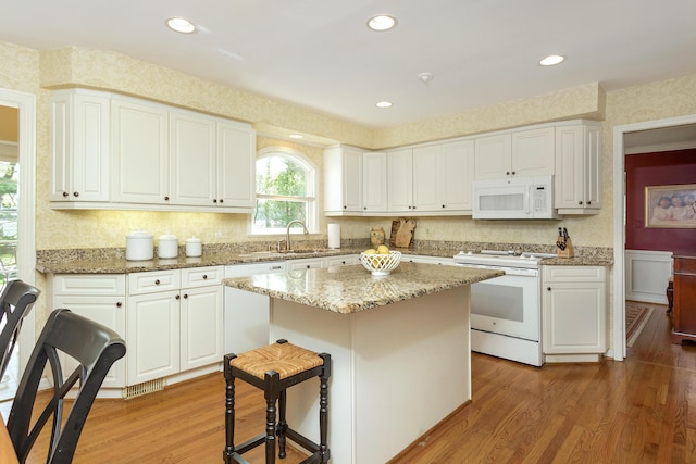 kitchen featuring a center island, light stone counters, white cabinets, white appliances, and light wood-style flooring