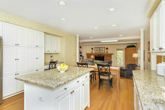 kitchen with white cabinets, a fireplace, light wood-style floors, open floor plan, and decorative columns