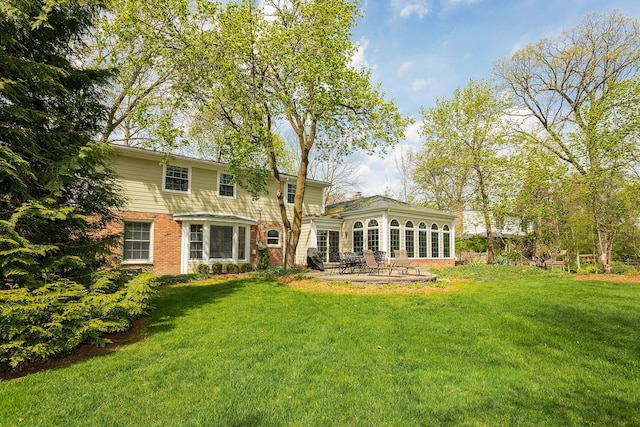 back of house featuring brick siding, a patio area, a yard, and a sunroom