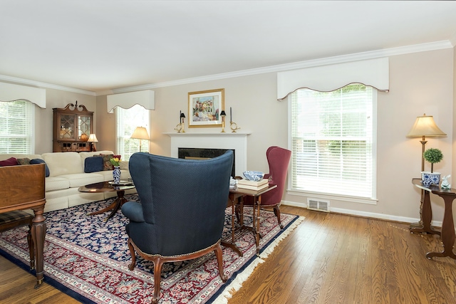 living area with visible vents, baseboards, crown molding, and wood finished floors