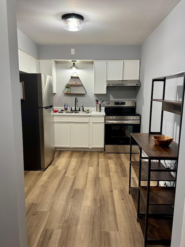 kitchen featuring under cabinet range hood, white cabinets, a sink, light wood finished floors, and stainless steel appliances