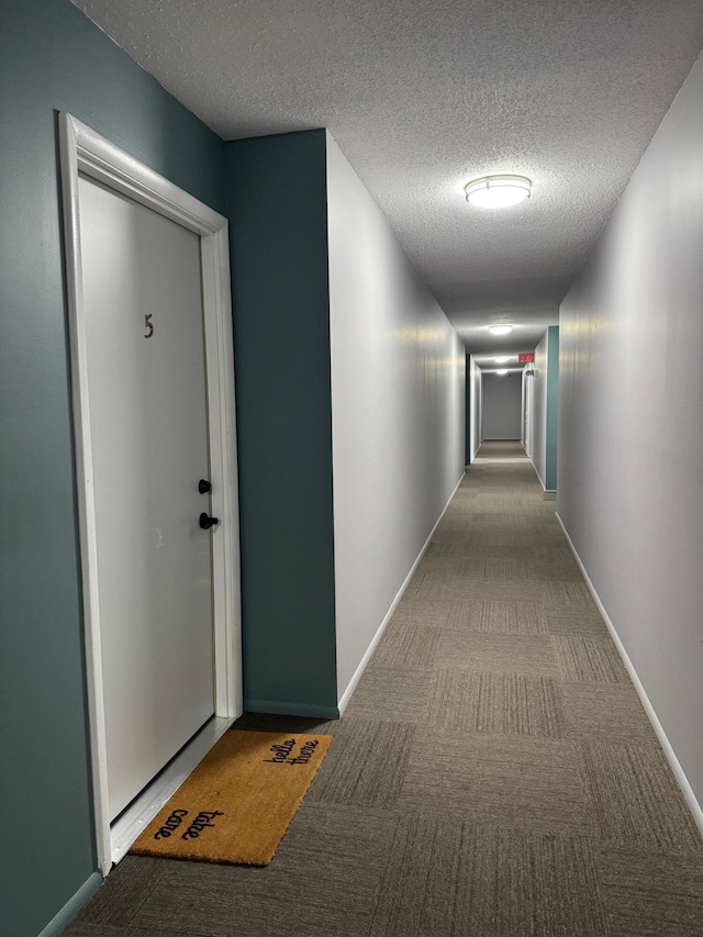 hallway with a textured ceiling, baseboards, and carpet