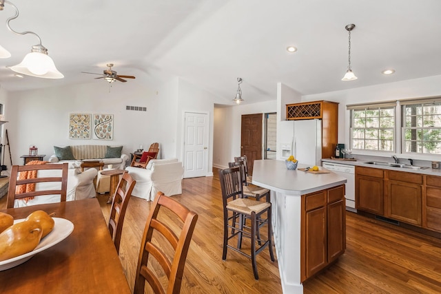 kitchen with white appliances, a kitchen breakfast bar, brown cabinetry, lofted ceiling, and visible vents