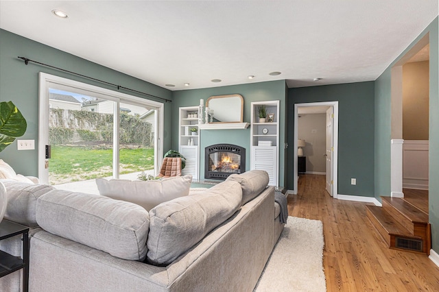 living room featuring a glass covered fireplace, light wood-style flooring, recessed lighting, baseboards, and visible vents