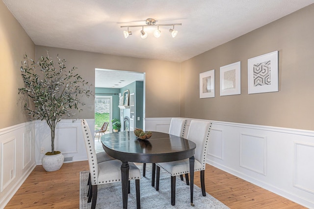 dining area with a decorative wall, wainscoting, light wood-type flooring, and visible vents