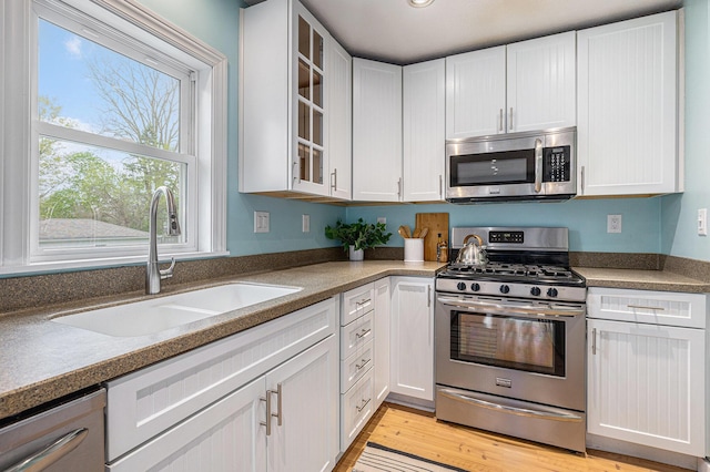 kitchen with a sink, glass insert cabinets, white cabinets, and stainless steel appliances