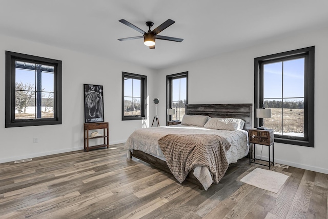 bedroom featuring baseboards, visible vents, multiple windows, and wood finished floors