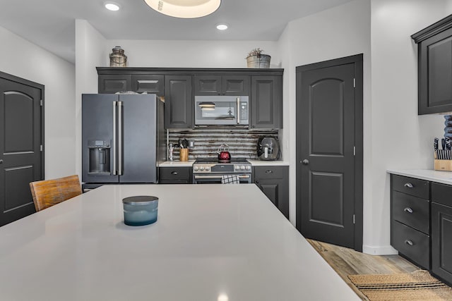 kitchen featuring light countertops, backsplash, wood finished floors, and stainless steel appliances
