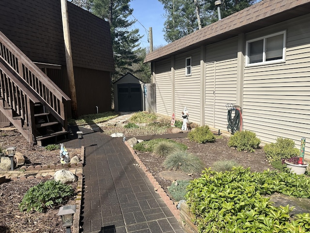 view of property exterior with a shed, roof with shingles, an outbuilding, and stairway