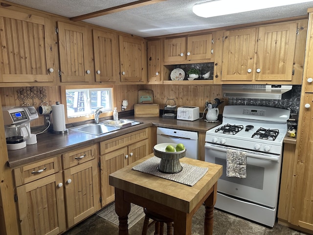 kitchen with a sink, under cabinet range hood, white appliances, and a textured ceiling