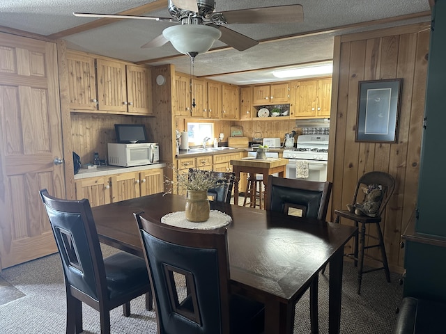 carpeted dining area with wooden walls, a textured ceiling, ceiling fan, and a sink