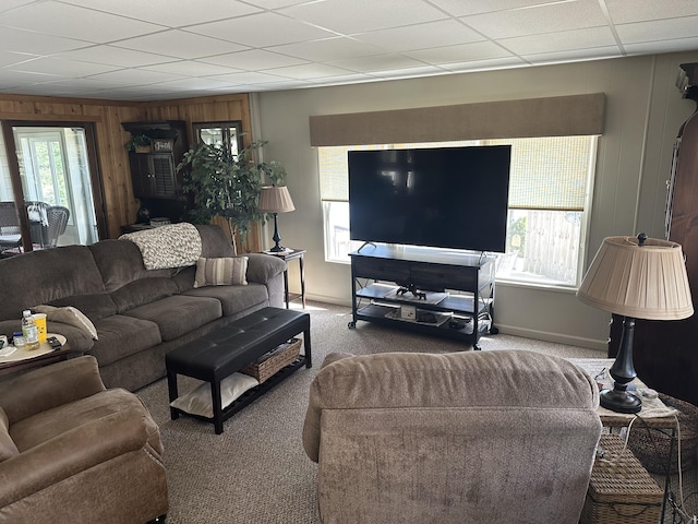 carpeted living area featuring wooden walls, baseboards, and a drop ceiling