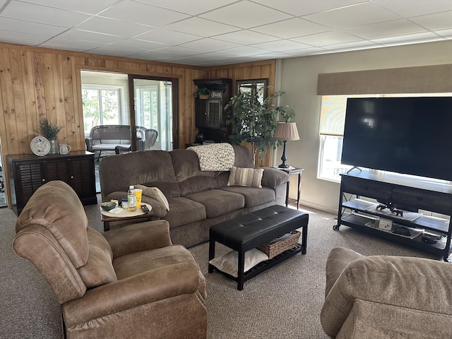 carpeted living room with wooden walls and a paneled ceiling