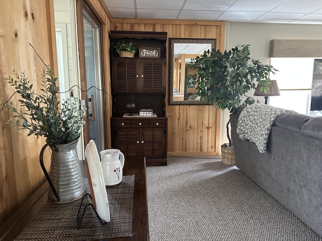 carpeted living area featuring wooden walls and a drop ceiling