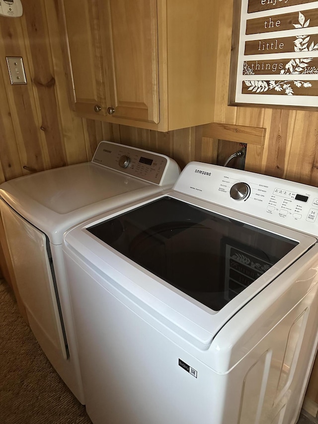 laundry room with cabinet space, separate washer and dryer, and wooden walls