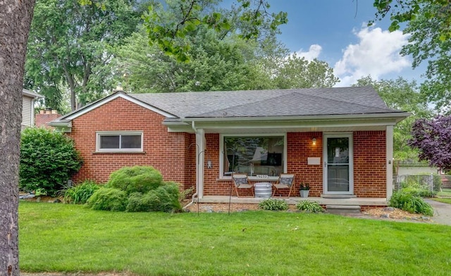ranch-style home featuring covered porch, a shingled roof, a front lawn, and brick siding