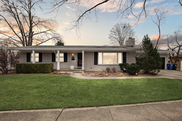 ranch-style home featuring covered porch, driveway, a chimney, brick siding, and a yard