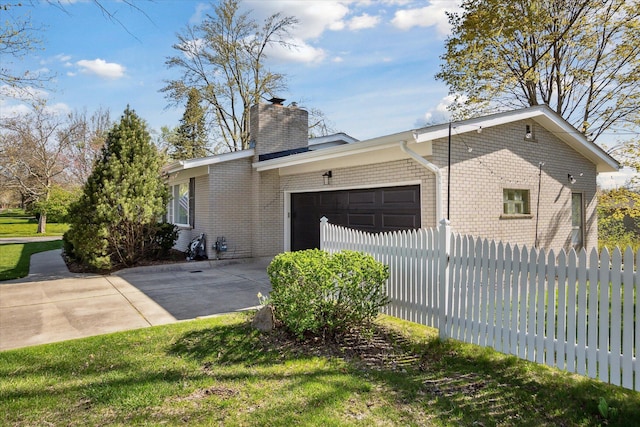 view of home's exterior featuring fence, a chimney, brick siding, an attached garage, and driveway