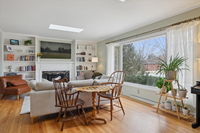living room with a skylight, built in features, a fireplace, and light wood finished floors