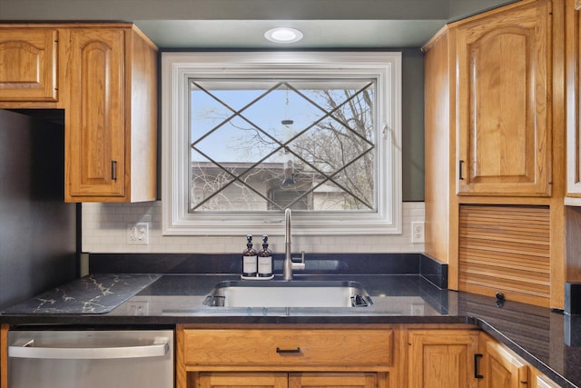 kitchen with stainless steel dishwasher, backsplash, a sink, and dark stone counters