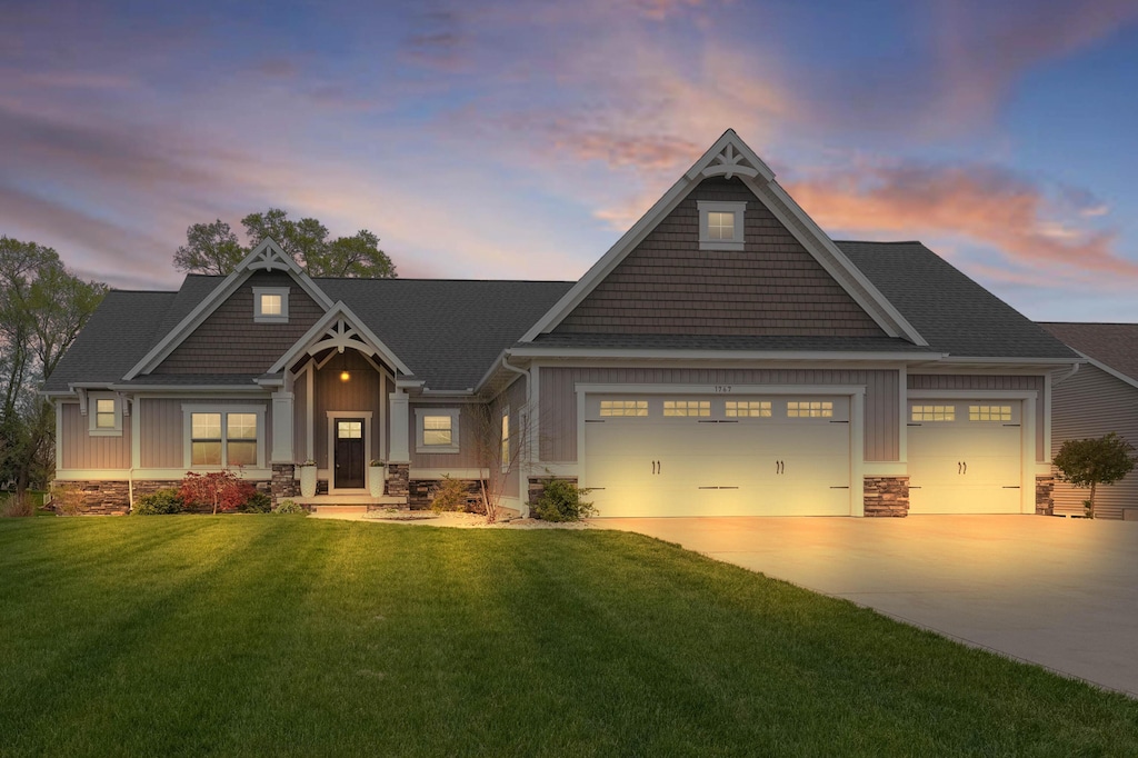 craftsman-style house with a front lawn, stone siding, board and batten siding, an attached garage, and driveway