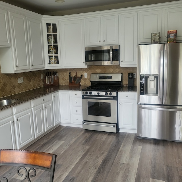 kitchen featuring dark stone counters, dark wood finished floors, white cabinetry, glass insert cabinets, and appliances with stainless steel finishes