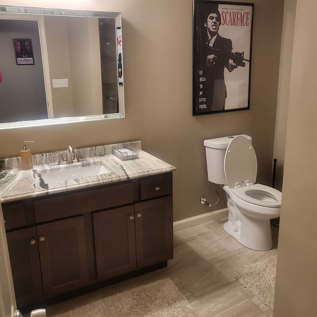 half bathroom with baseboards, vanity, and toilet