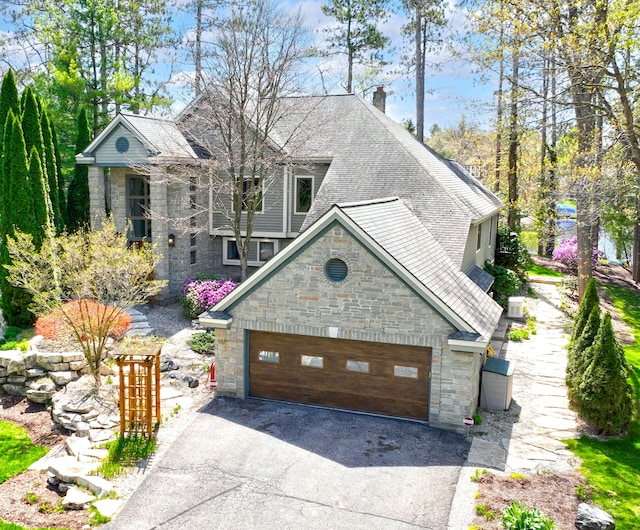 view of front of house with a chimney, roof with shingles, driveway, and stone siding