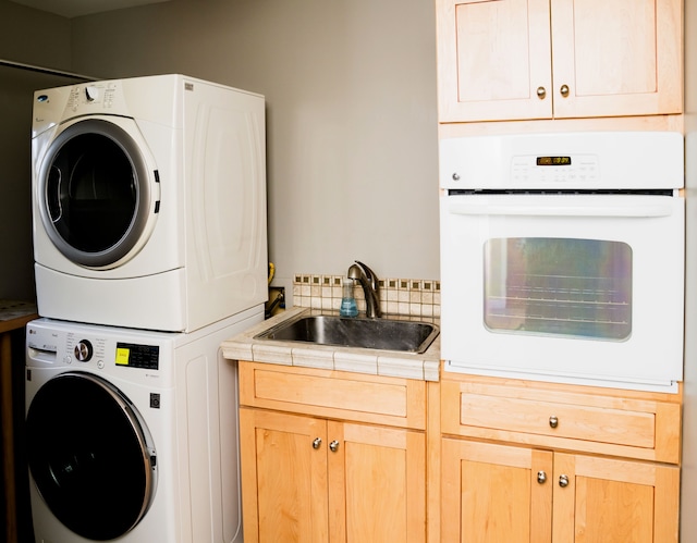 washroom with stacked washing maching and dryer, laundry area, and a sink