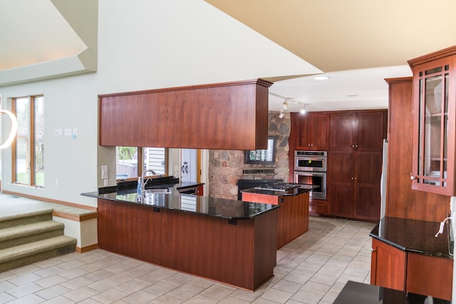kitchen featuring stainless steel double oven, a sink, a peninsula, glass insert cabinets, and dark stone counters
