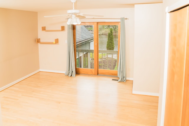spare room featuring a ceiling fan, baseboards, wood finished floors, and a water view