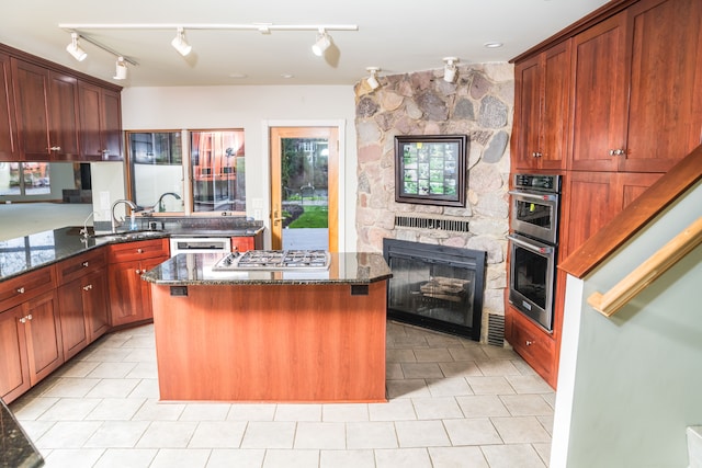 kitchen featuring appliances with stainless steel finishes, a sink, a fireplace, dark stone countertops, and a center island