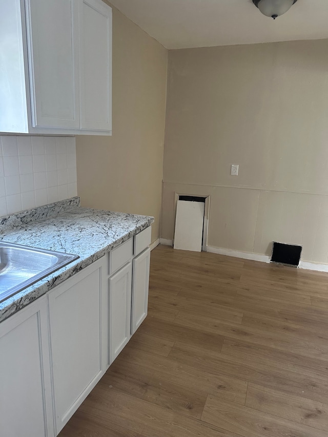 kitchen with light stone countertops, light wood-type flooring, white cabinetry, a sink, and backsplash