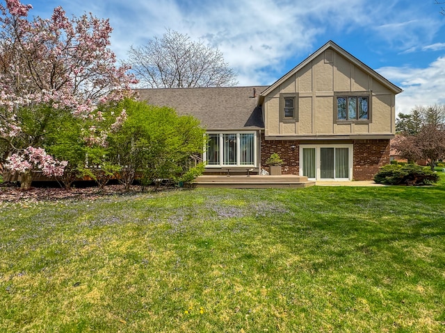 back of property with brick siding, a lawn, and a deck