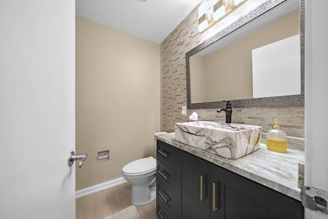 half bathroom featuring vanity, wood finished floors, toilet, baseboards, and tasteful backsplash