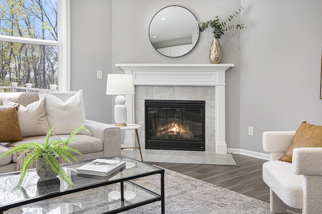 living room with a tiled fireplace, baseboards, and wood finished floors