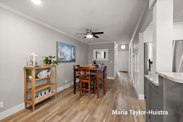 dining space featuring baseboards, ornamental molding, a ceiling fan, and light wood finished floors