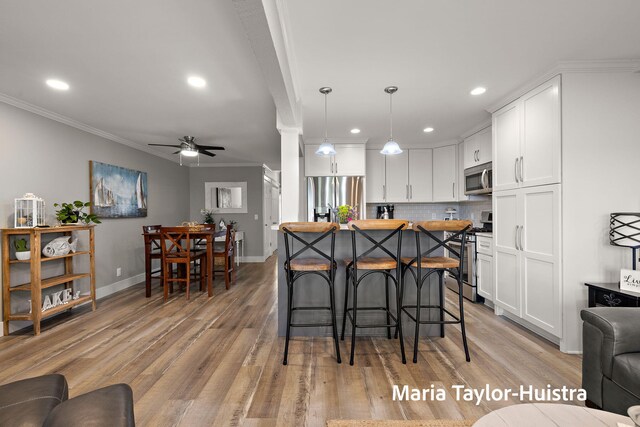 kitchen featuring crown molding, a kitchen bar, white cabinetry, a ceiling fan, and stainless steel appliances