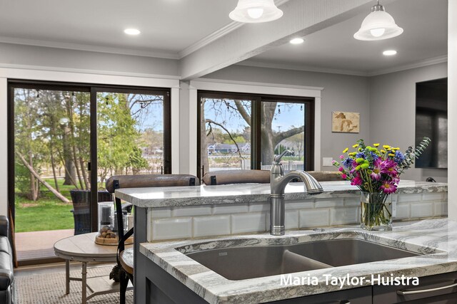 kitchen featuring ornamental molding, recessed lighting, light stone counters, a sink, and decorative light fixtures