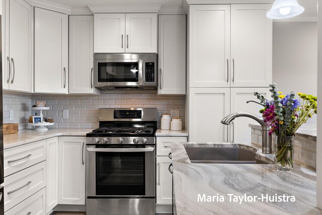 kitchen featuring backsplash, appliances with stainless steel finishes, a sink, light stone counters, and white cabinetry