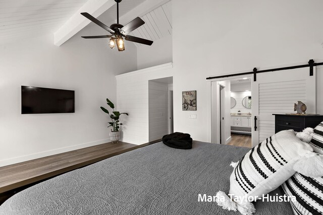 bedroom with beam ceiling, a barn door, wood finished floors, and high vaulted ceiling