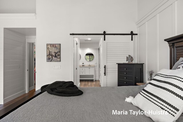 bedroom with wood finished floors, a high ceiling, a barn door, a sink, and ensuite bath