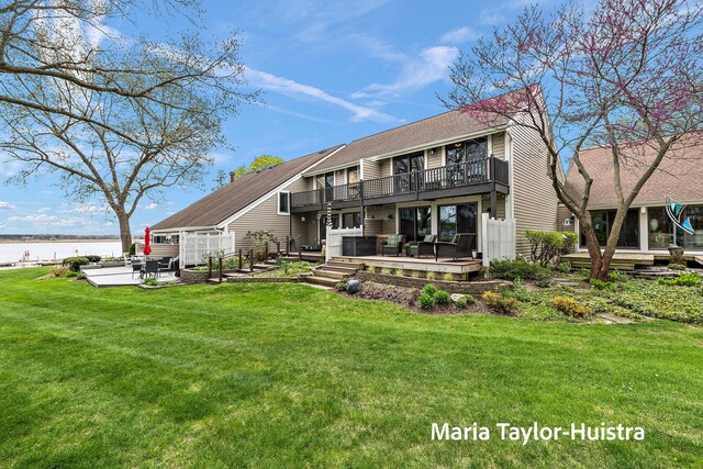 back of property featuring a balcony, a patio, roof with shingles, a lawn, and a water view