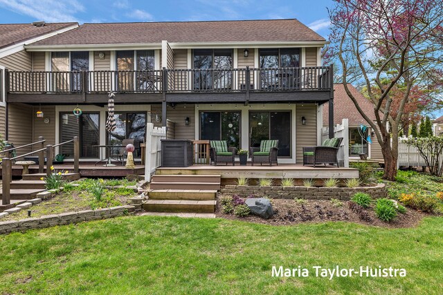 back of property with a lawn, a deck, a shingled roof, and a balcony