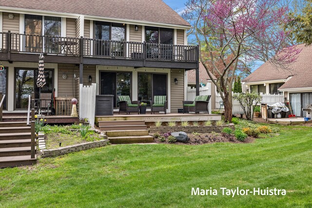 back of property with a lawn, a shingled roof, and a balcony